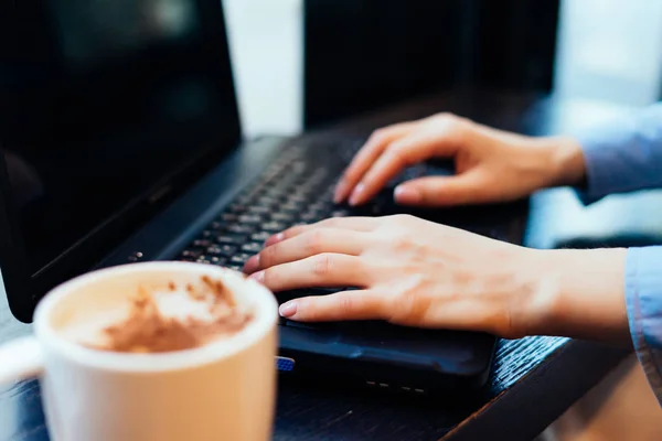 Девушка фрилансер в синей рубашке работает на ноутбуке в кафе, рядом с кружка с ароматным кофе — стоковое фото