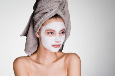 Kafasındaki bir havlu ile genç bir kız yüzünü temizlemek için beyaz bir maske uygulanan
