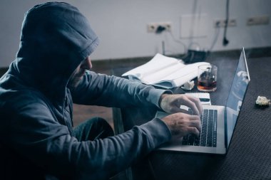 genç adam hacker ile başını kaputa bir kazak'ı bir dizüstü oturur
