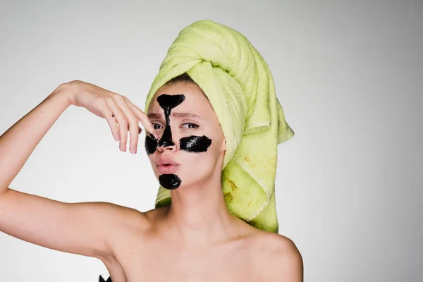 Ένα νεαρό κορίτσι με μια πετσέτα στο κεφάλι της εφαρμόζεται μια μαύρη μάσκα για να καθαρίσει το δέρμα προβλήματος — Φωτογραφία Αρχείου
