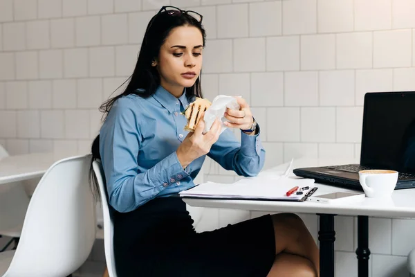 Üzletasszony irodájában ül a fehér asztalnál, kávét inni és enni egy szendvicset — Stock Fotó