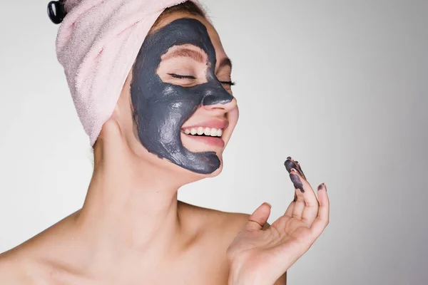 Szczęśliwa młoda dziewczyna po prysznic z ręcznikiem na głowie stosuje się oczyszczanie maski na twarz — Zdjęcie stockowe