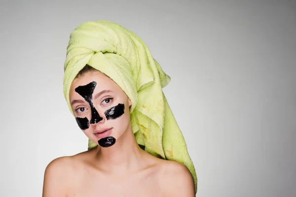 A young girl with a towel on her head applied a black mask to clean the skin of her face — Stock Photo, Image