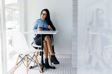 mavi bir gömlek ve gözlük dersten sonra bir kafede otururken kendine güvenen düşünceli kız öğrenci