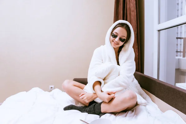 Niña sonriente se despertó temprano, con una bata de terciopelo blanco, bajo los ojos de manchas negras, sentado en la cama —  Fotos de Stock