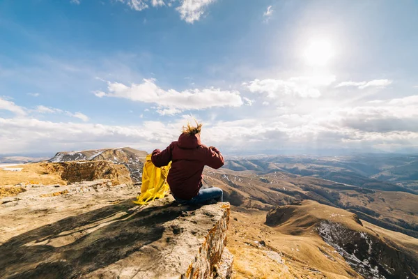 Молодая девушка ведет здоровый и активный образ жизни, сидит на краю горы с желтым рюкзаком — стоковое фото
