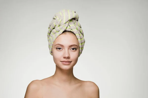 Selbstbewusstes junges Mädchen mit sauberer Haut, mit einem grünen Handtuch auf dem Kopf, das in die Kamera blickt — Stockfoto