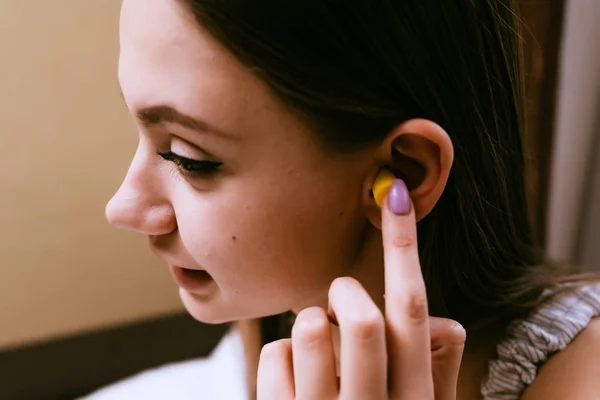 Ένα χαριτωμένο νεαρή κοπέλα θέλει να κοιμηθεί, εισάγει στα αυτιά της κίτρινο ωτοασπίδες κατά το θόρυβο οδών — Φωτογραφία Αρχείου