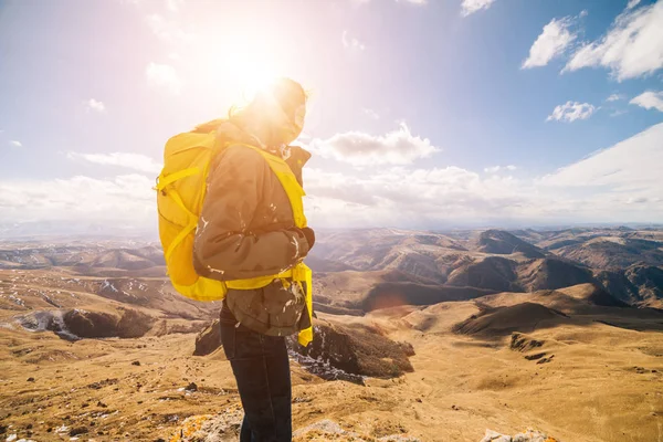 La niña viaja a través de las montañas caucásicas con una mochila amarilla, en los rayos del sol —  Fotos de Stock