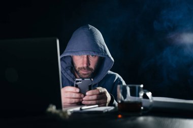 gizemli sakallı adam karanlıkta bir smartphone, hacks, yüzünü başlık altında gizler