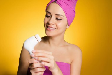 güzel kız başında pembe havlu ile gülümseyen yüzünü derin temizleme için elektrikli bir fırça tutar