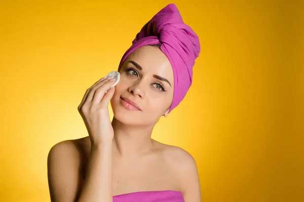 Ελκυστική νεαρή κοπέλα με μια ροζ πετσέτα στο κεφάλι της καθαρίζει το πρόσωπό της με ένα δίσκο βαμβακιού — Φωτογραφία Αρχείου