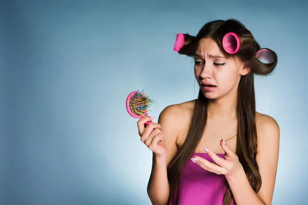 Молодая грустная девушка теряет волосы, держит расческу, на голове бигуди — стоковое фото
