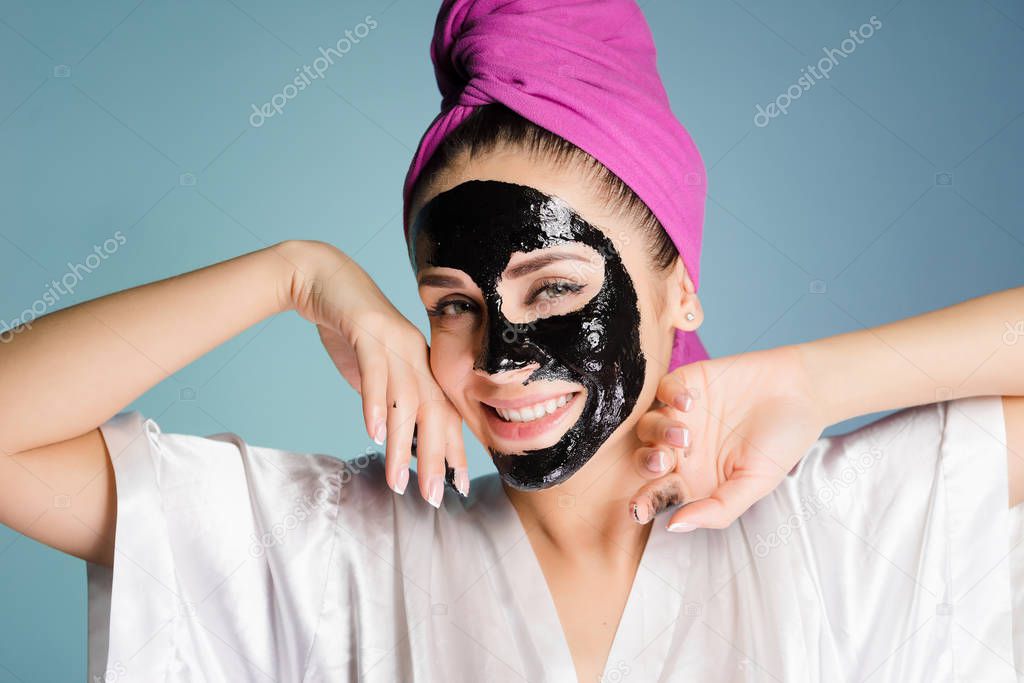 happy smiling girl with white teeth, with a pink towel on her head, applied a black cleansing mask on her face