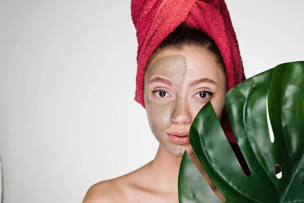 Uma linda jovem com uma toalha vermelha na cabeça aplicou uma máscara de barro — Fotografia de Stock