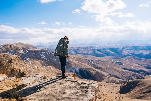 Una jovencita viaja, se encuentra al borde de una montaña y disfruta de la naturaleza, mira hacia abajo —  Fotos de Stock