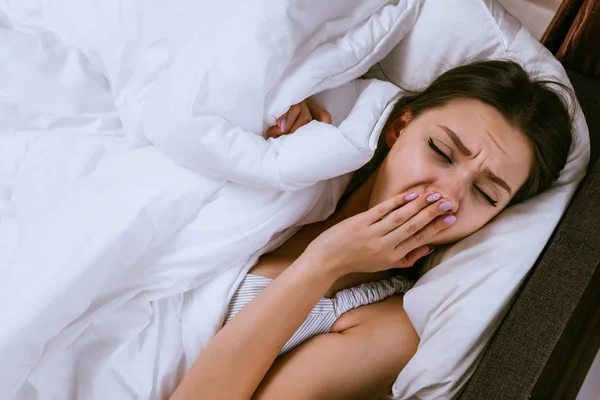 sleepy young girl woke up early, does not want to get up, lies under a white blanket