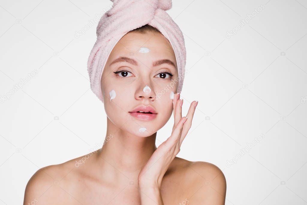 young beautiful girl with a pink towel on her head puts on face moisturizer