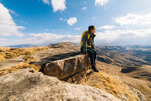 Egy aktív fiatal lány, egy túra a kaukázusi ridge, ül a szélén egy sziklán, és ellazítja — Stock Fotó