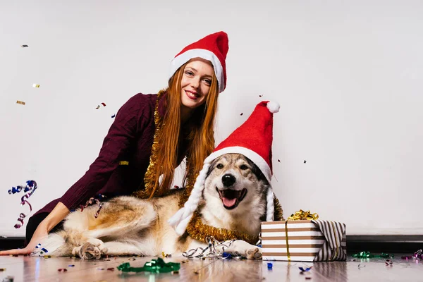 Joyeuse fille rousse dans une casquette rouge célèbre la nouvelle année avec son gros chien — Photo