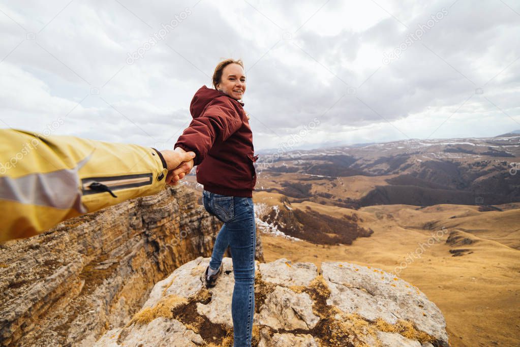 happy young girl holding a guy by the hand, traveling through the Caucasus mountains