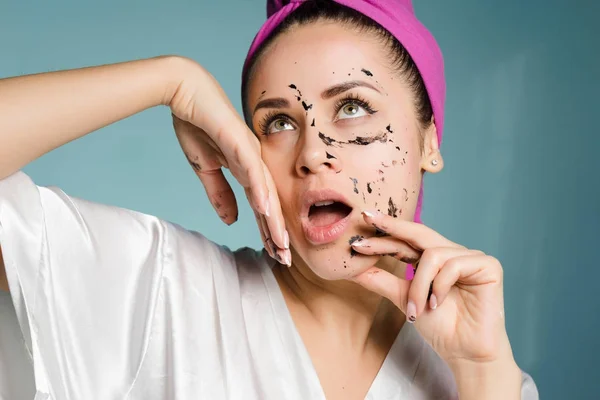 Αστείο κορίτσι με μια ροζ πετσέτα στο κεφάλι της αφαιρεί ένα μαύρο καθαρισμού μάσκα από το πρόσωπό της — Φωτογραφία Αρχείου