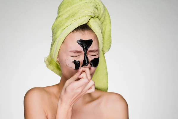 En ung flicka med en grön handduk på hennes huvud tar bort en svart mask från hennes ansikte, det gör ont — Stockfoto