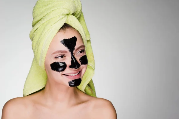 Felice ragazza con un asciugamano verde sulla testa applicato una maschera di pulizia nera sul suo viso — Foto Stock