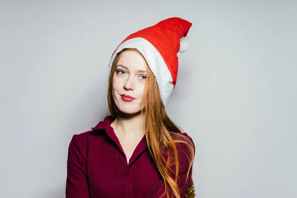 Schöne rothaarige Mädchen in einer roten Mütze wie Santa Claus wartet auf ein neues Jahr — Stockfoto