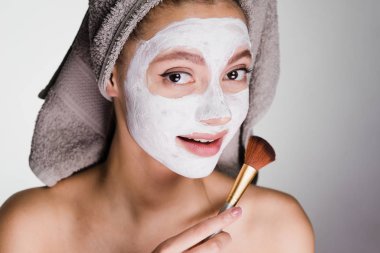 Kafasındaki bir havlu ile çekici kız bir beyaz nemlendirici maske bir fırça ile uygulanan