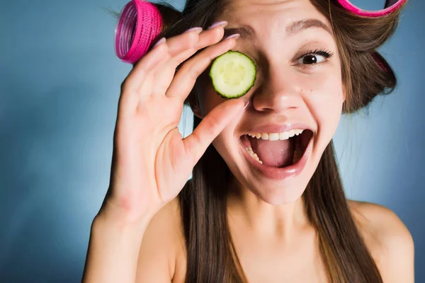 Cildi nemlendirmek için gülümseyen kız curlers kafasındaki bir dilim salatalık holding ile — Stok fotoğraf
