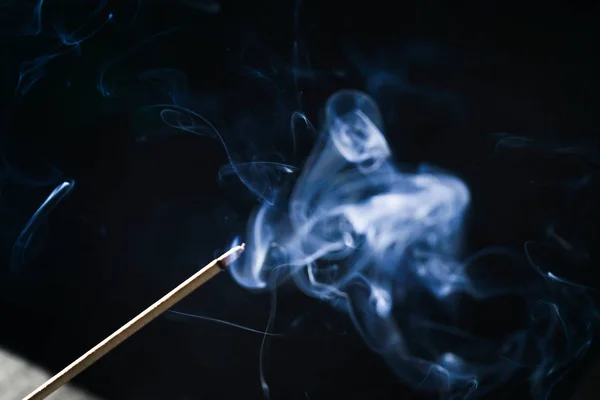 Ароматическая палка тлеет в темноте, голубом дыме — стоковое фото