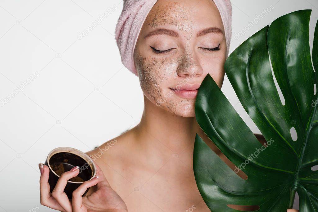 attractive beautiful girl with a towel on her head applied to her face a coffee scrub, enjoying spa treatments