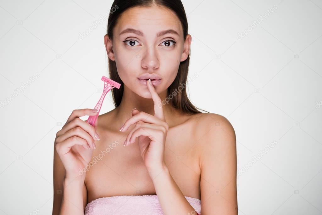 a young attractive girl holds a pink razor in her hands, put a finger to her lips