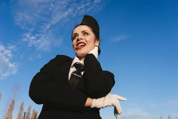 Смешная юная стюардесса в форме показывает язык, на фоне голубого неба — стоковое фото