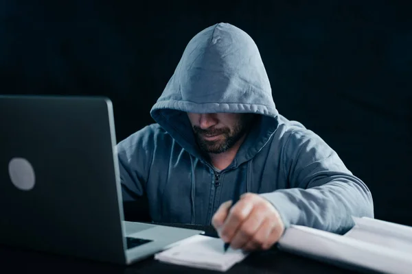 Pria misterius menyeringai meng-hack laptop, menyembunyikan wajahnya di bawah kap — Stok Foto