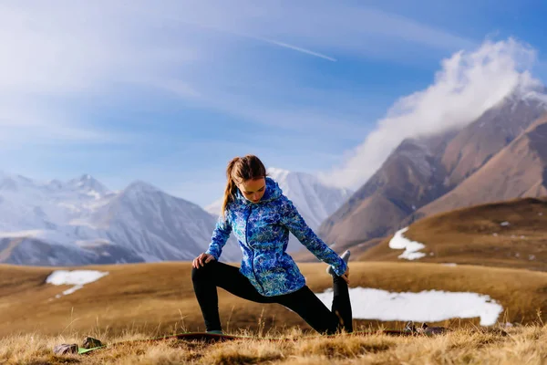 Активная девушка в синей куртке занимается йогой на фоне Кавказских гор — стоковое фото