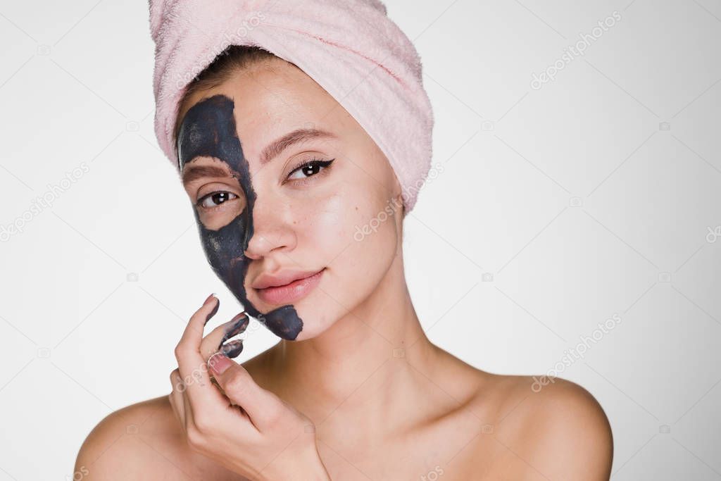 an attractive young girl with a pink towel on her head applied a clay useful mask to half the face