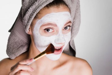 bir havlu ile güzel güzel kız beyaz bir besleyici maske yüzü bir fırça ile uygulanan