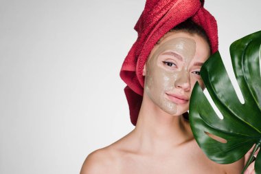 başında kırmızı bir havlu ile çekici bir kız bir kil maskesi yarım yüz için bir spa prosedür uygulanır.