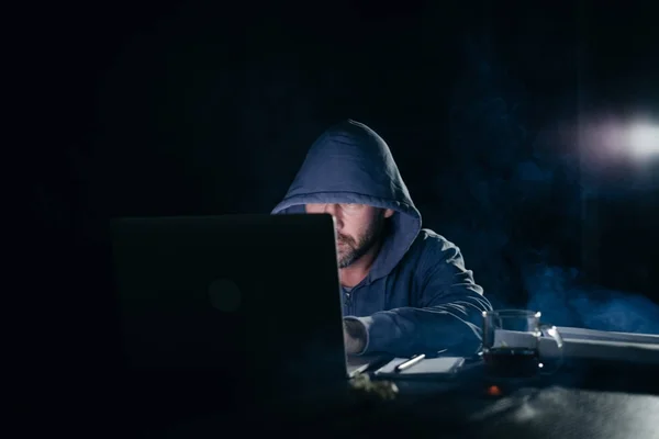 Homme criminel mystérieux dans un capot pirate un ordinateur portable dans le noir — Photo