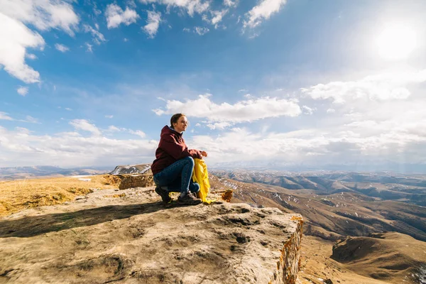 Активна молода дівчина сидить на краю скелі і насолоджується гірським повітрям і сонцем — стокове фото