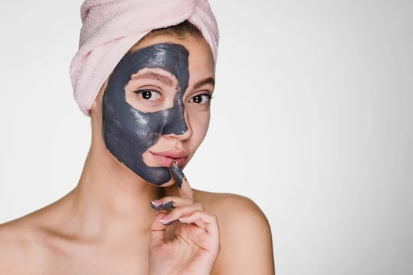 A young smiling girl with a pink towel on her head applied a clay mask to half the face — Stock Photo, Image