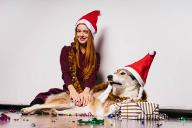 Kızıl saçlı kız büyük köpeğiyle yılbaşı atmosfer, Noel Baba gibi kırmızı bir yumruk başında oturur