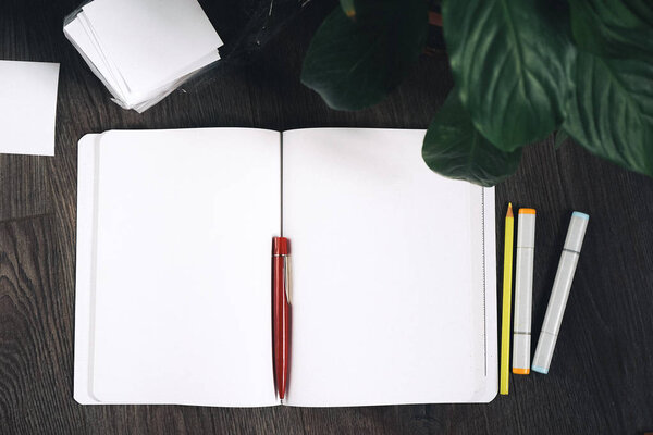 on a wooden floor lies a notebook with clean white sheets and a red pen,