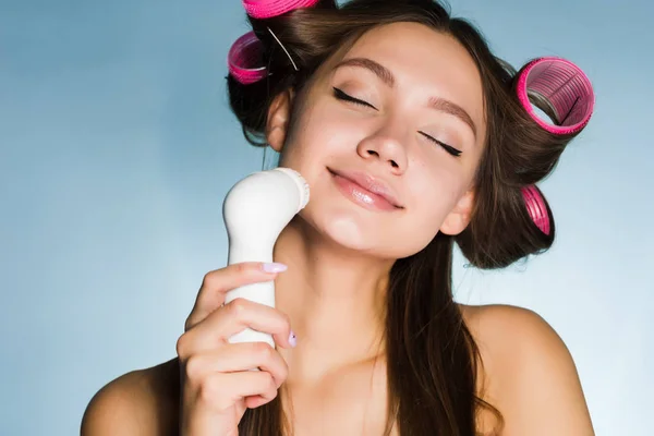 Ένα χαριτωμένο νεαρή κοπέλα με σίδερα στο κεφάλι της κάνει ένα βαθύ καθαρισμό του δέρματος προσώπου με τη βοήθεια του μια ηλεκτρική βούρτσα — Φωτογραφία Αρχείου