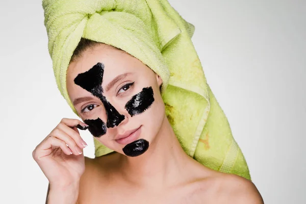 Härlig tjej med en grön handduk på huvudet tillämpa en svart mask mot akne på problemområden i ansiktet — Stockfoto