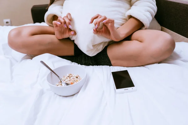 Das Mädchen sitzt in warmen Socken auf einem Bett und frühstückt Haferbrei — Stockfoto