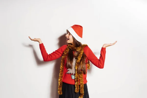 Hermosa chica sorprendida en una gorra roja como Santa Claus y en un suéter de Año Nuevo está esperando la Navidad —  Fotos de Stock