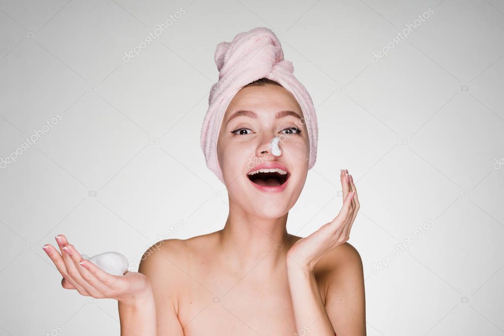 happy young girl with a pink towel on her head applying a cleansing foam on her face